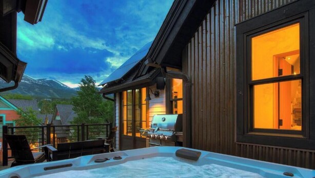 Een hottub met een houten terras en een barbecue, omgeven door een houten hek en uitzicht op een berg.