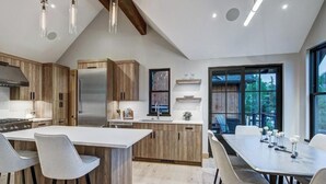 Een moderne keuken met houten kastjes, een centraal eiland, barkrukken en een eettafel met stoelen.