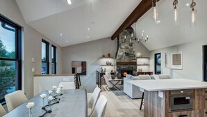 Een moderne keuken met een stenen open haard, een eethoek met een grote tafel en stoelen, en een zithoek met banken en een salontafel.
