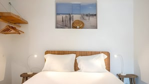 Une chambre avec un grand lit, deux oreillers, une tête de lit en bois, une fenêtre donnant sur la plage et deux lampes de chevet.