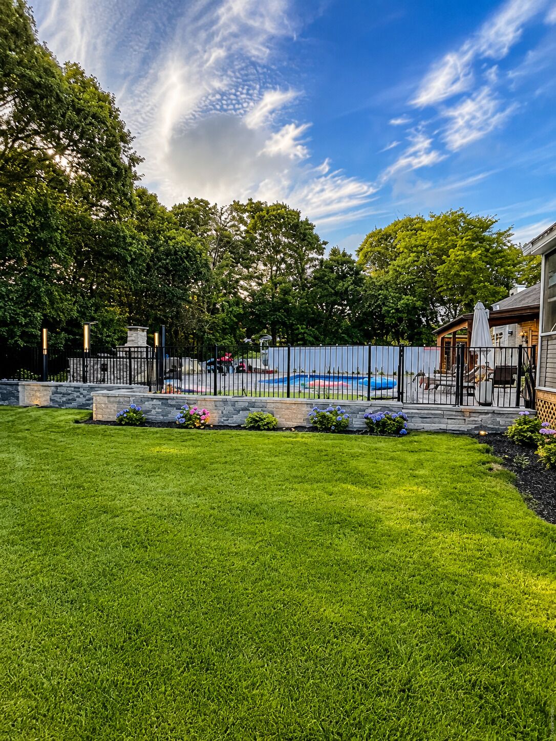 A backyard with a swimming pool, a stone fountain, and a wooden deck.