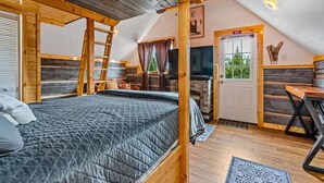 Un dormitorio estilo loft acogedor con una cama grande, vigas de madera, chimenea y una pequeña zona de cocina.