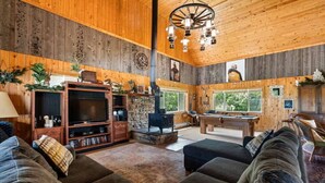 Un acogedor interior de cabaña con chimenea, paredes de madera, mesa de billar y una zona de estar confortable.