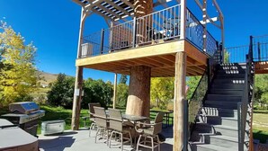Una terraza de madera con pérgola, mobiliario exterior y una parrilla.