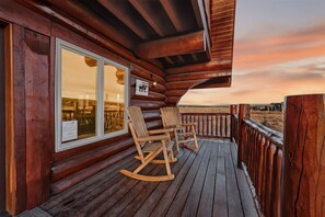 A wooden deck with rocking chairs and a view of the sunset. - Buckskin Flats | Sleeps 18! By the Lake! Boat Ramp, Hot Tub, & AC! (Island Park)