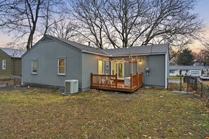 Ein kleines, eingeschossiges Haus mit Veranda und Terrasse, umgeben von Bäumen und einem Rasen.