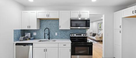 Een moderne keuken met witte kasten, een roestvrijstalen vaatwasser, een zwart fornuis en een magnetron.
