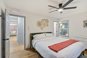 Ein Schlafzimmer mit Bett, Deckenventilator, Fenster und einer Tür zu einem anderen Raum.