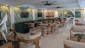 Un restaurant moderne avec des tables et des chaises en bois, des sièges rembourrés de tissu vert, des ventilateurs de plafond et un coin bar.