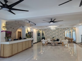 Vestíbulo de hotel con mostrador de recepción, zona de estar, ventiladores de techo y pared decorada.