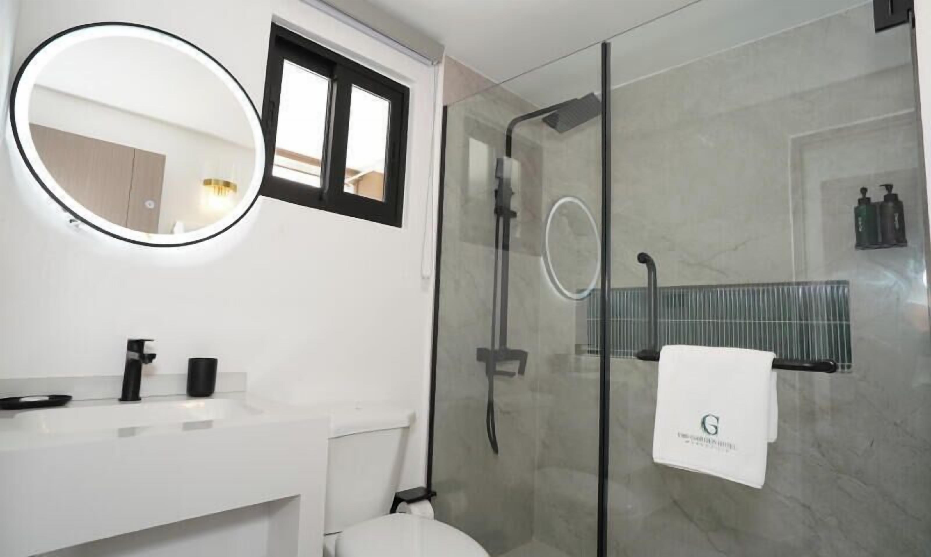 Un baño moderno con ducha de vidrio, un espejo redondo y un lavamanos blanco.