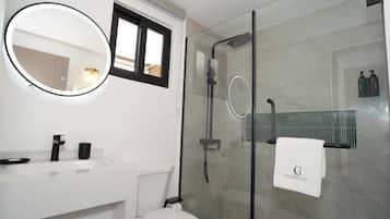 Un baño moderno con ducha de vidrio, un espejo redondo y un lavamanos blanco.