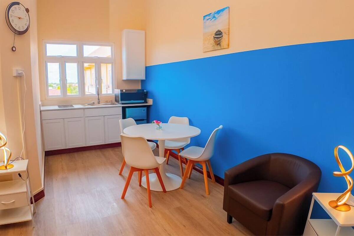 A compact living space with a kitchenette, a dining area with a round table and chairs, a sofa, and a decorative lamp.