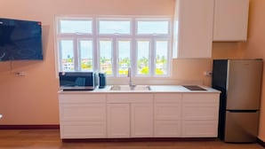 A kitchen with a window, a microwave, a sink, and a refrigerator. - MDG Suites (Uitvlugt)