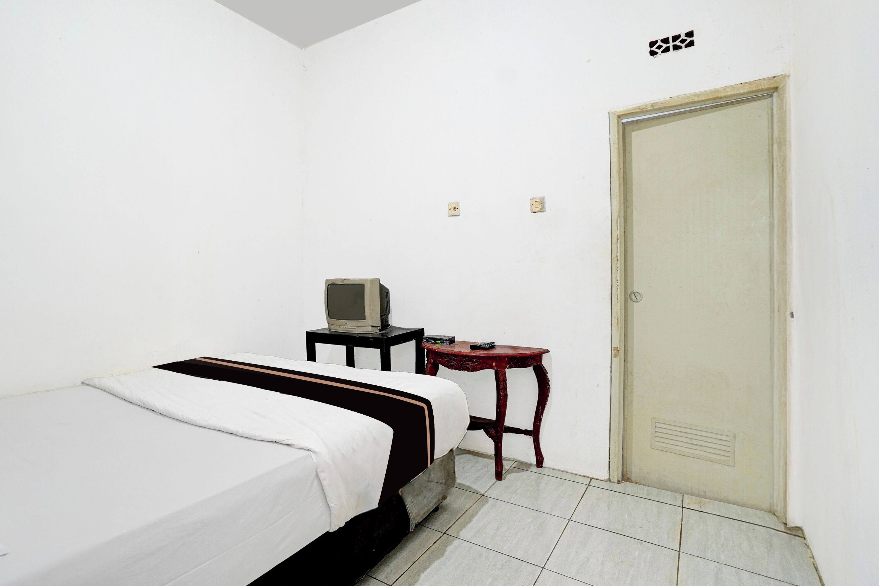 A small, simple room with a bed, a television on a small table, and a door.
