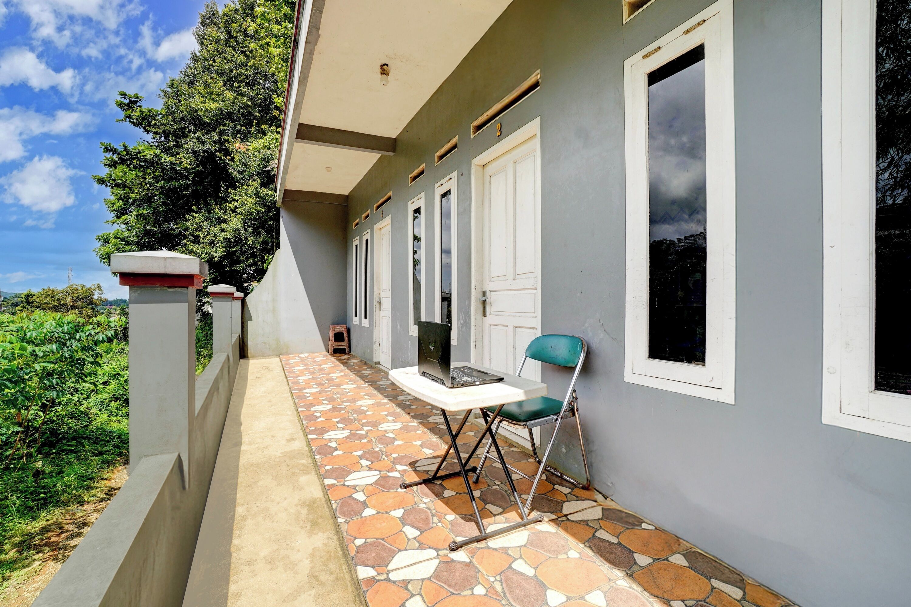 A covered outdoor area with a tiled floor, a table with a laptop, and a chair.