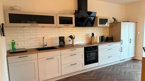 Une cuisine moderne avec des meubles blancs, une hotte noire et un parquet en bois disposé en chevrons.