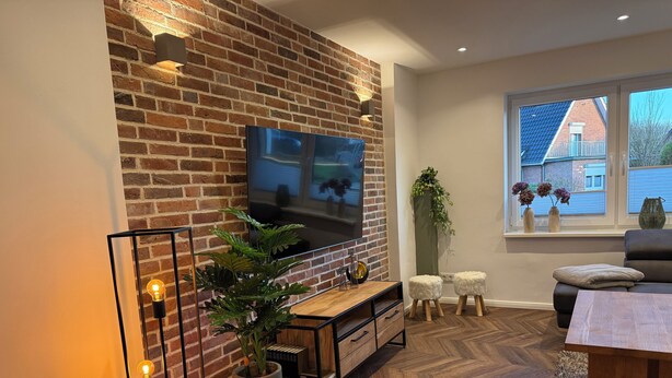 Un salon moderne avec un mur en briques, un téléviseur à écran plat, une table basse en bois et une grande plante en pot.