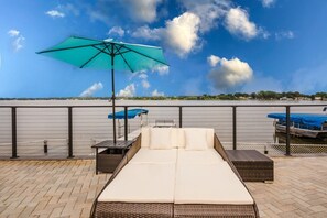 Una terraza en la azotea con vista a una masa de agua, un área de descanso con sofá y sillones, y un paraguas grande.