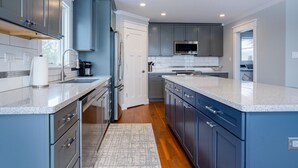 A modern kitchen with grey cabinets, stainless steel appliances, and a granite countertop.