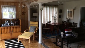 Un accogliente soggiorno con pavimento in legno, un tappeto a righe, una poltrona gialla, un tavolo da pranzo con sedie e un lampadario.