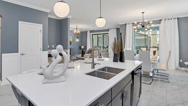 A modern kitchen with a white island, stainless steel sink, and contemporary lighting fixtures. - Pool & BBQ - Disney-Themed Cozy 6BD - Near Disney (Kissimmee)