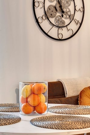A clear glass vase with oranges on a table, a wall clock with gears, and a brown sofa with a beige throw blanket. - The Perfect Getaway for Couples (Firenze)