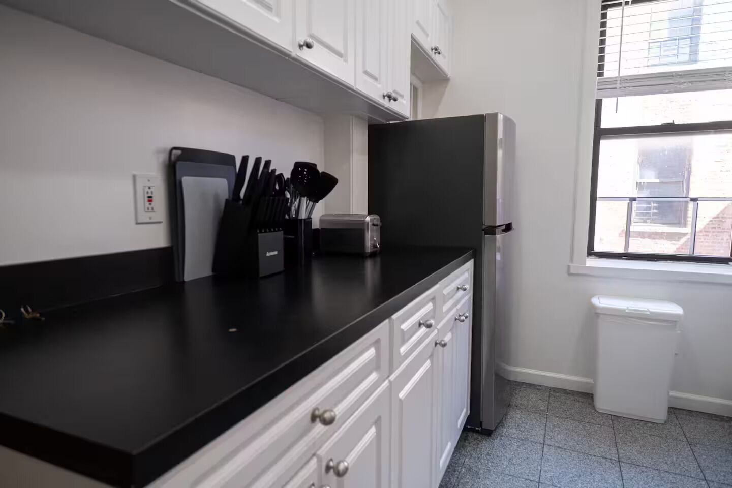 A kitchen with white cabinets, a black countertop, and a stainless steel refrigerator.