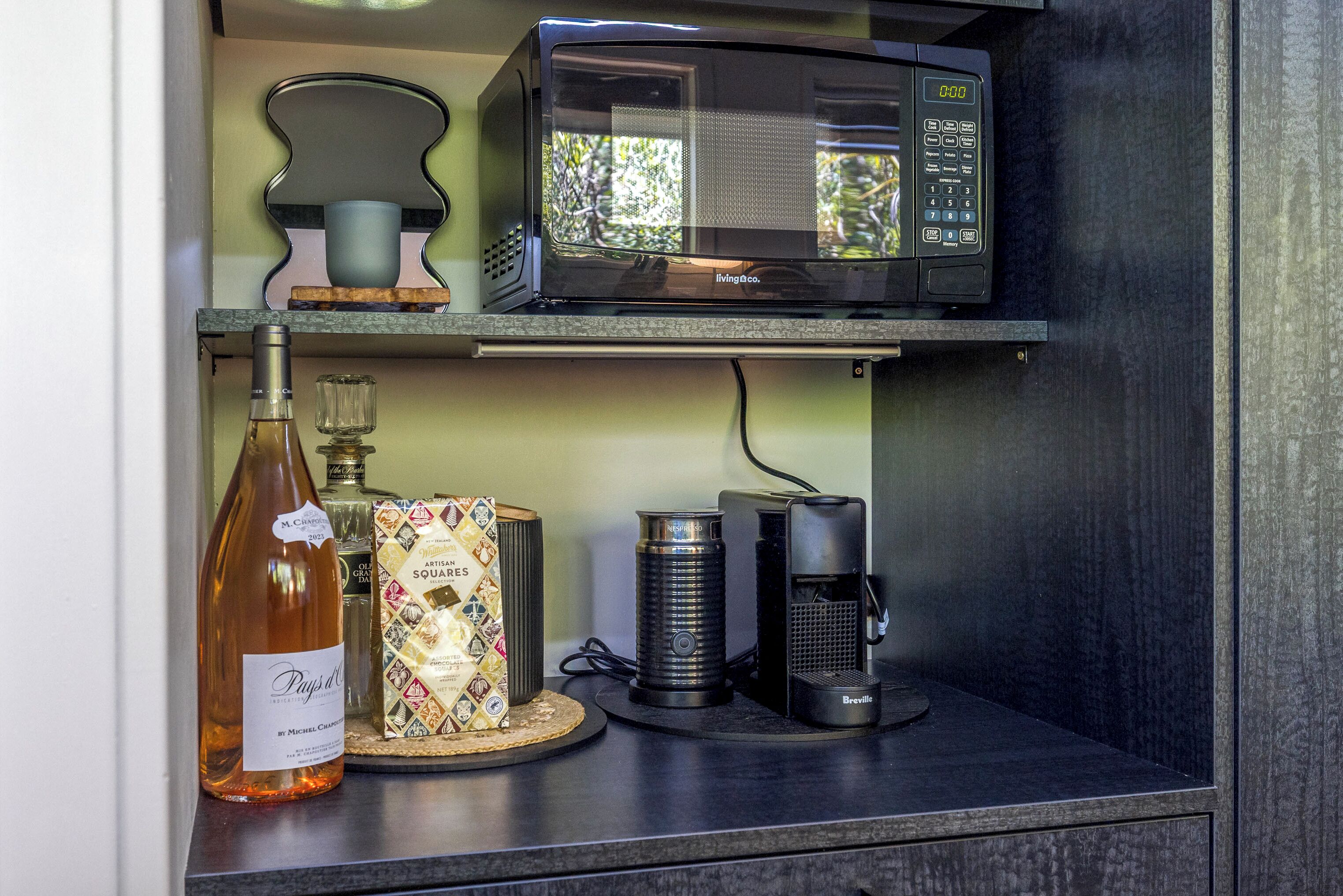 A kitchen counter with a microwave, a coffee maker, a bottle of wine, and a decorative box.