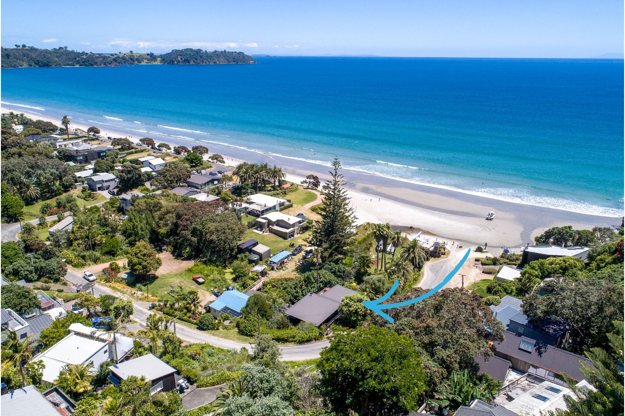 An aerial view of a coastal residential area with houses, a beach, and a clear blue ocean.