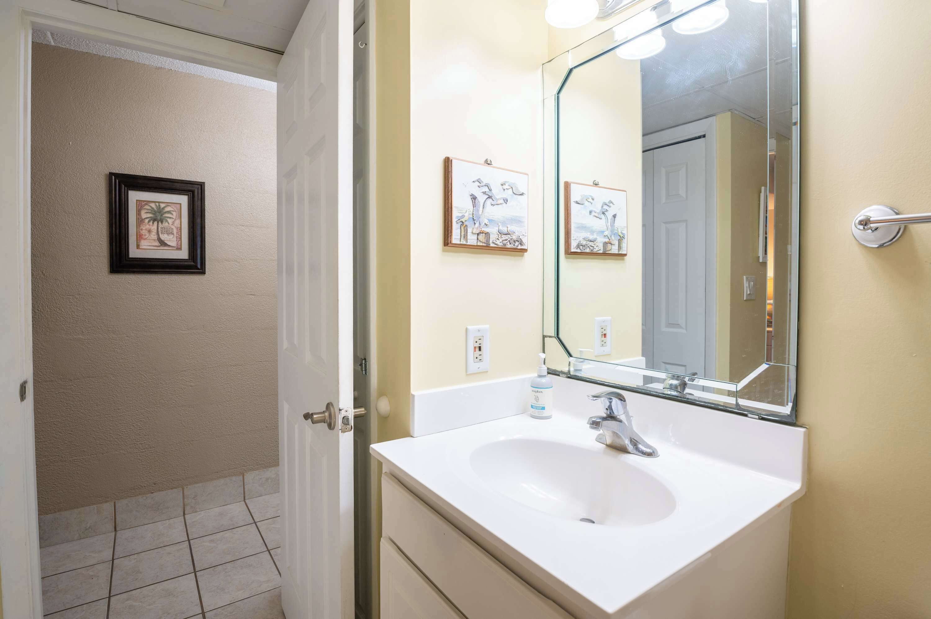 A bathroom with a white sink, a large mirror, and framed artwork on the wall.