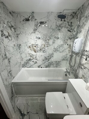 Une salle de bain avec un mur en marbre, une baignoire, une douche et des toilettes.