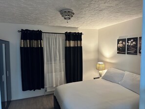 Une chambre à coucher avec un lit, une table de chevet, une lampe, un radiateur et une porte.