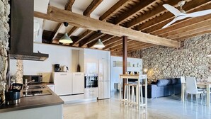 Une cuisine moderne avec des meubles blancs, un mur en pierre et un coin repas comprenant un canapé et une table.
