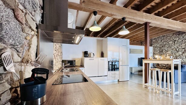 Une cuisine moderne dotée d’un îlot central, de murs en pierre et de poutres apparentes.