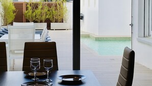 Un coin repas avec une table dressée pour deux personnes, donnant sur une piscine et un jardin.