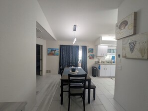 A dining area with a table and chairs, a kitchen in the background, and artwork on the walls.