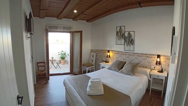 A bedroom with a large bed, two bedside tables with lamps, a wooden ceiling, and a view of an outdoor balcony. - CASA RURAL TOLANCA. Near Toledo and Puy du Fou (Sonseca)