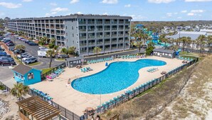 A hotel with a large swimming pool, multiple floors, and a parking lot. - Sun & Fun | Beachfront Resort~Pool~Lazy River~Gym (Myrtle Beach)