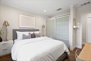 A modern bedroom with a large bed, bedside lamps, a nightstand, a wooden table, and a sliding glass door closet. - Walk to Google Cloud 10 min Google Main Campus (Sunnyvale)