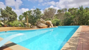 Una piscina rettangolare con acqua cristallina, circondata da una terrazza piastrellata e da grandi rocce.