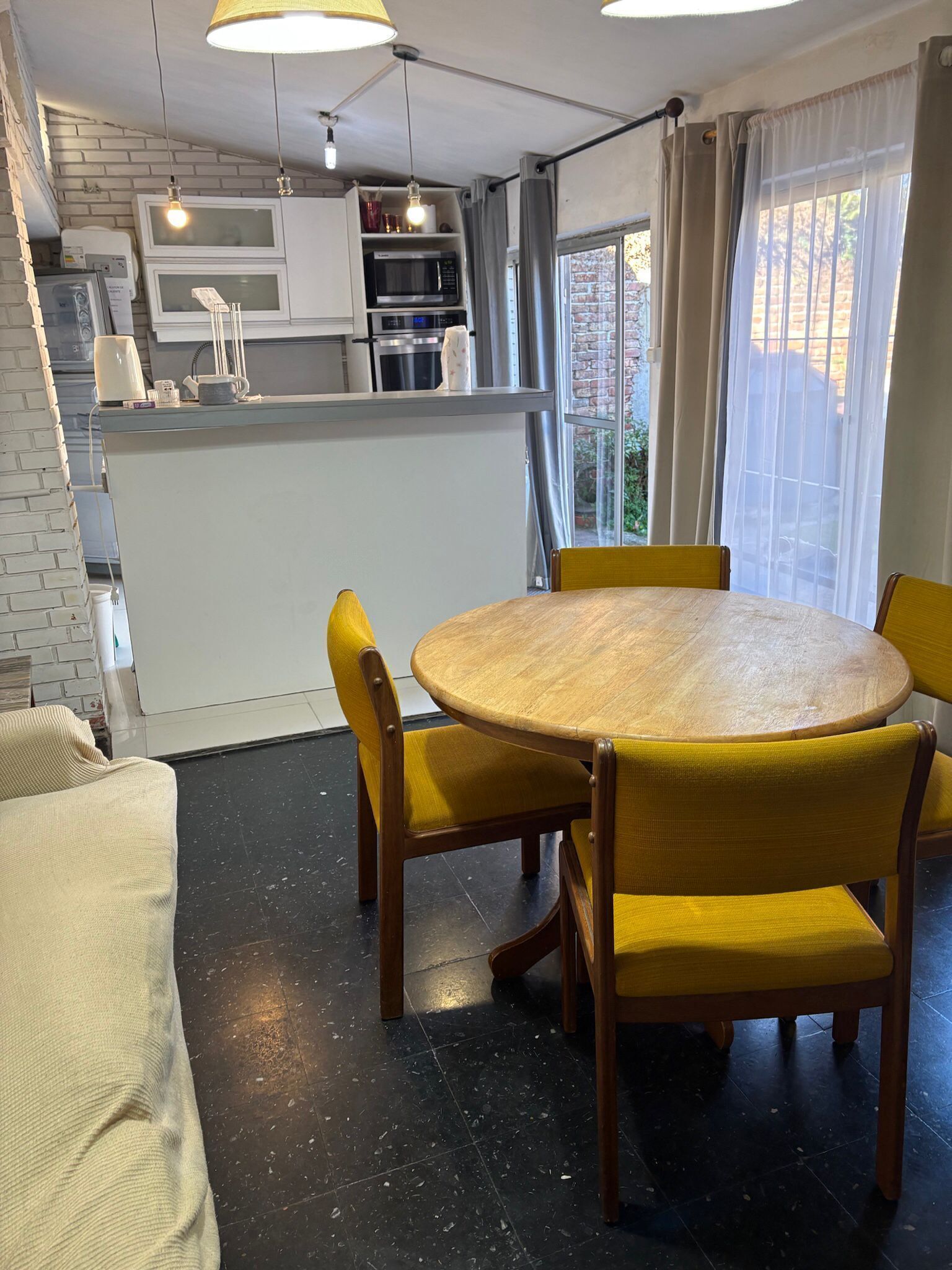 A compact kitchen with white cabinets, a microwave, and a kettle. There is a round wooden table with yellow chairs.