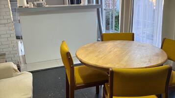A compact kitchen with white cabinets, a microwave, and a kettle. There is a round wooden table with yellow chairs.