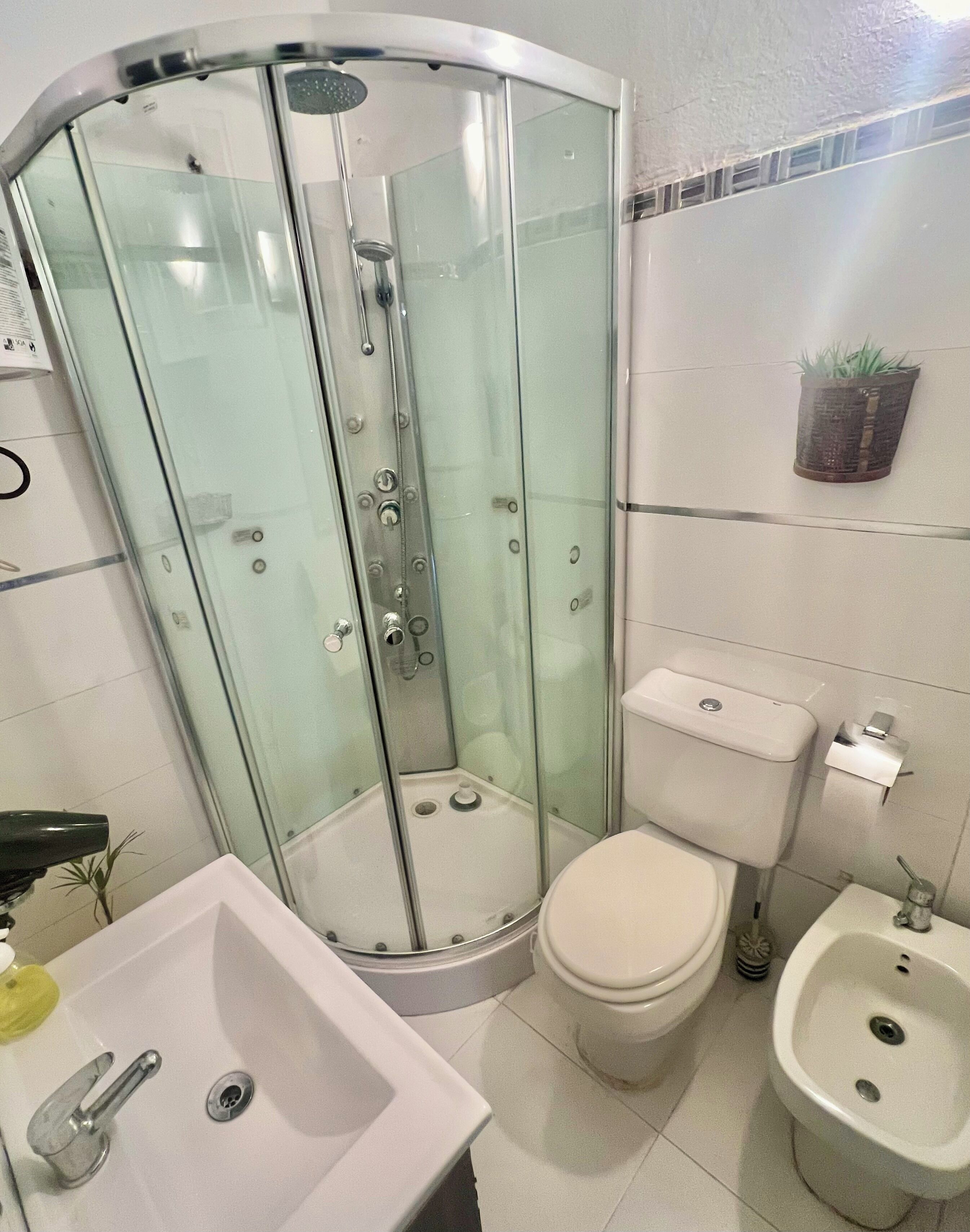 A modern bathroom with a glass-enclosed shower, a toilet, a bidet, and a sink.