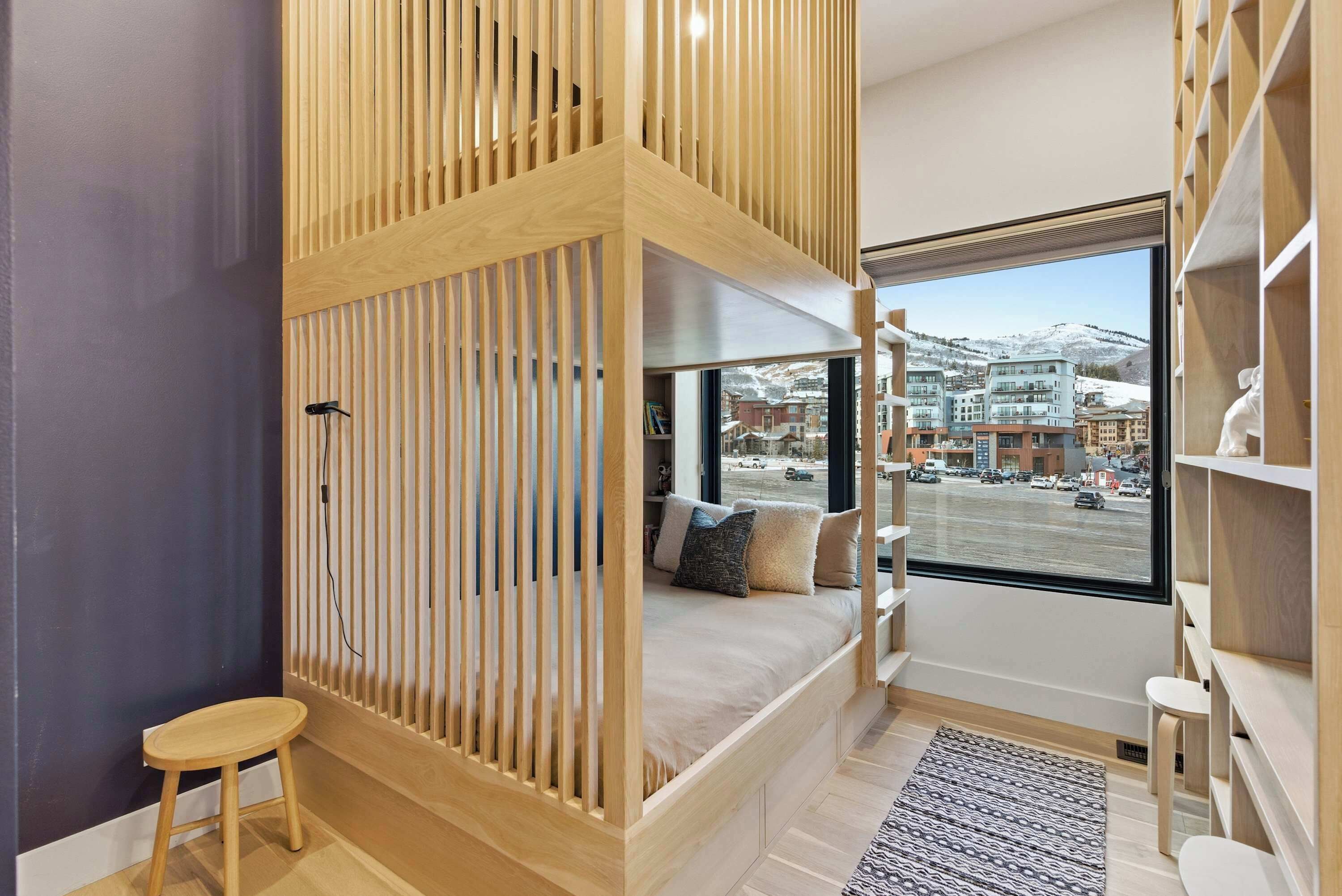 Una camera da letto moderna con un letto a scomparsa, una finestra vista città e una libreria in legno.
