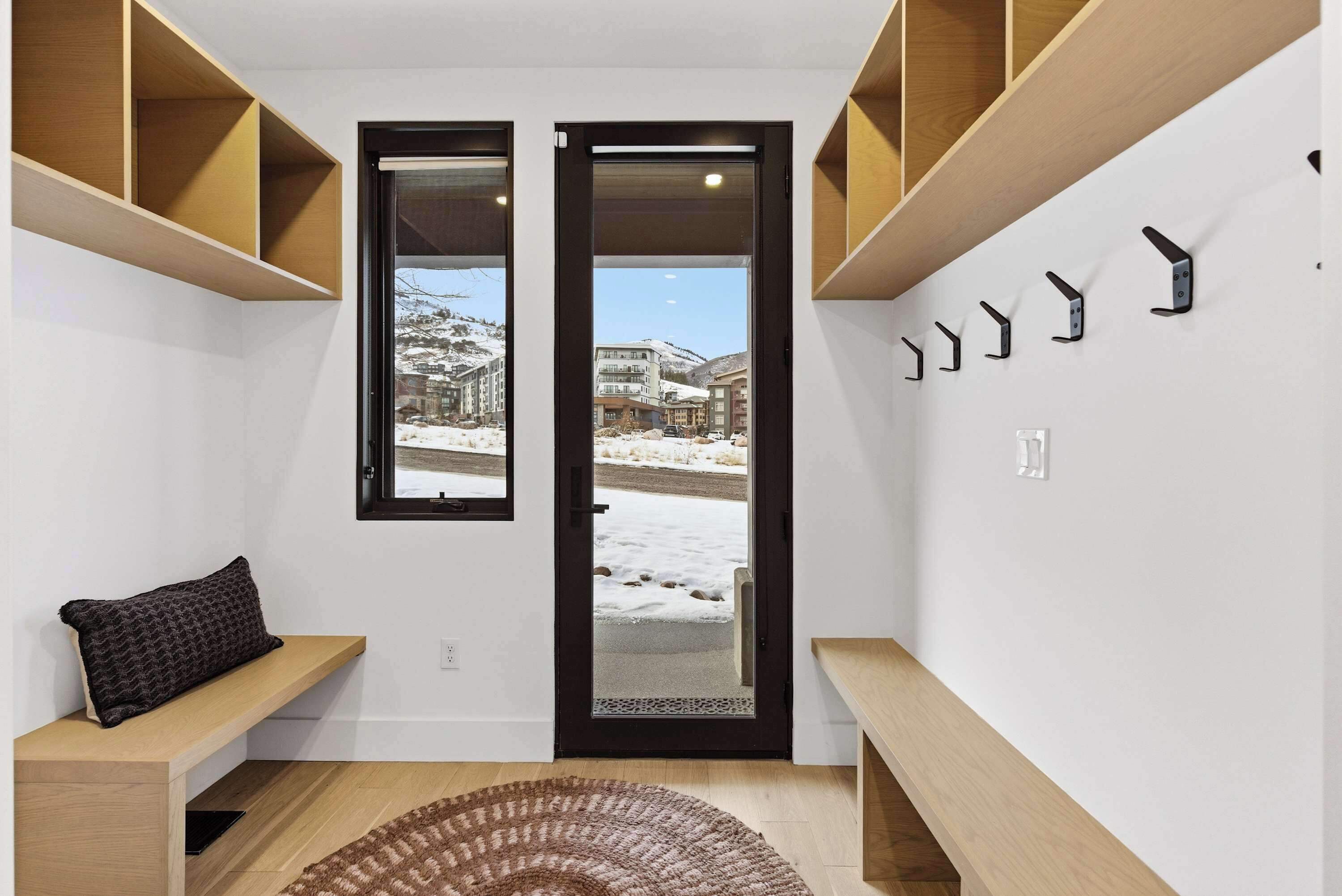 Un intérieur moderne avec un banc en bois, un tapis et une porte donnant sur un espace extérieur enneigé.
