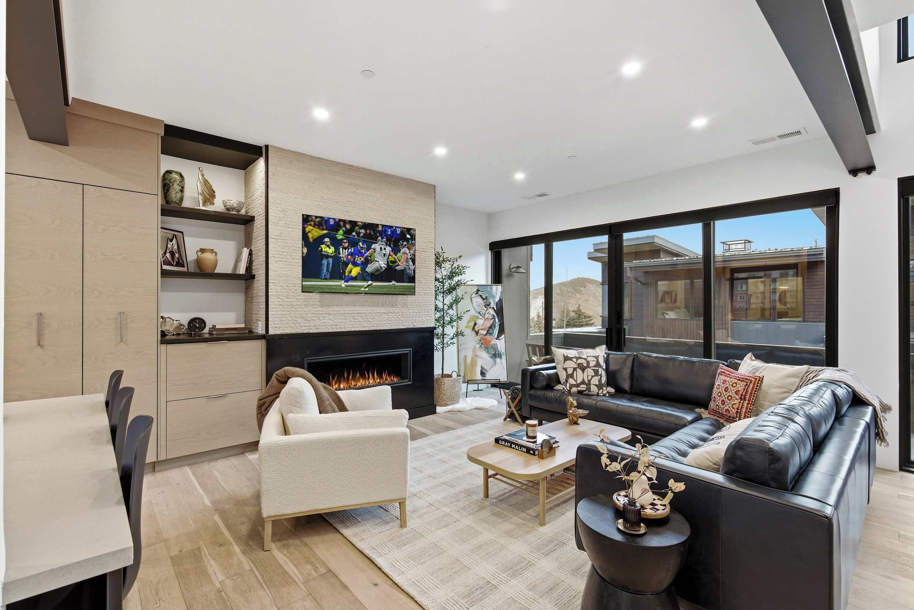 A modern living room with a fireplace, a black leather sofa, a white armchair, and a dining area with a table and chairs.