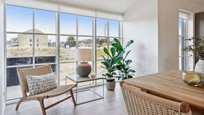 A spacious room with large windows, a wooden dining table, wicker chairs, a potted plant, and a lamp. - Cozy home in Løkken with WiFi (Løkken)
