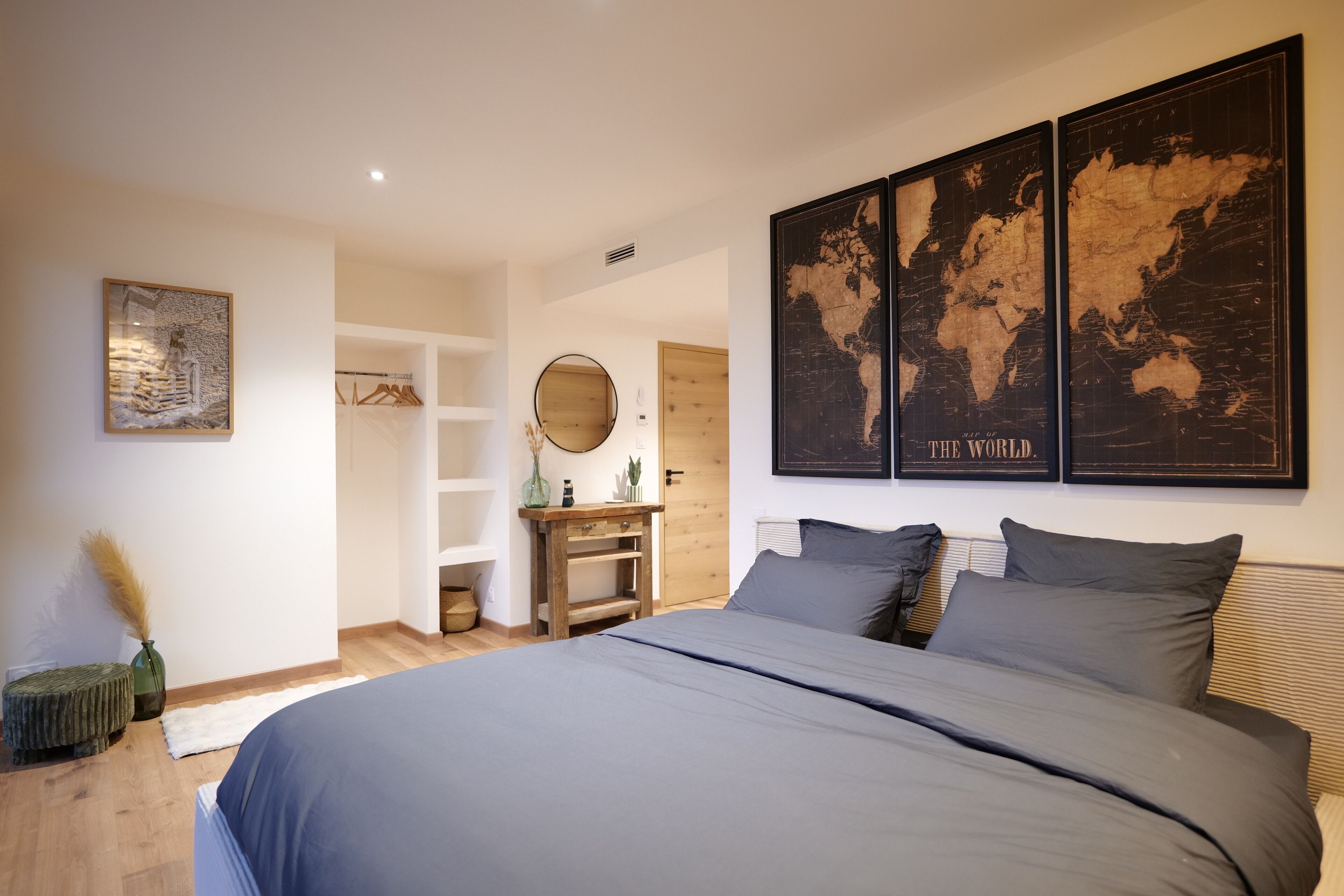 A bedroom with a large bed, a wooden dresser, a round mirror, and a world map on the wall.