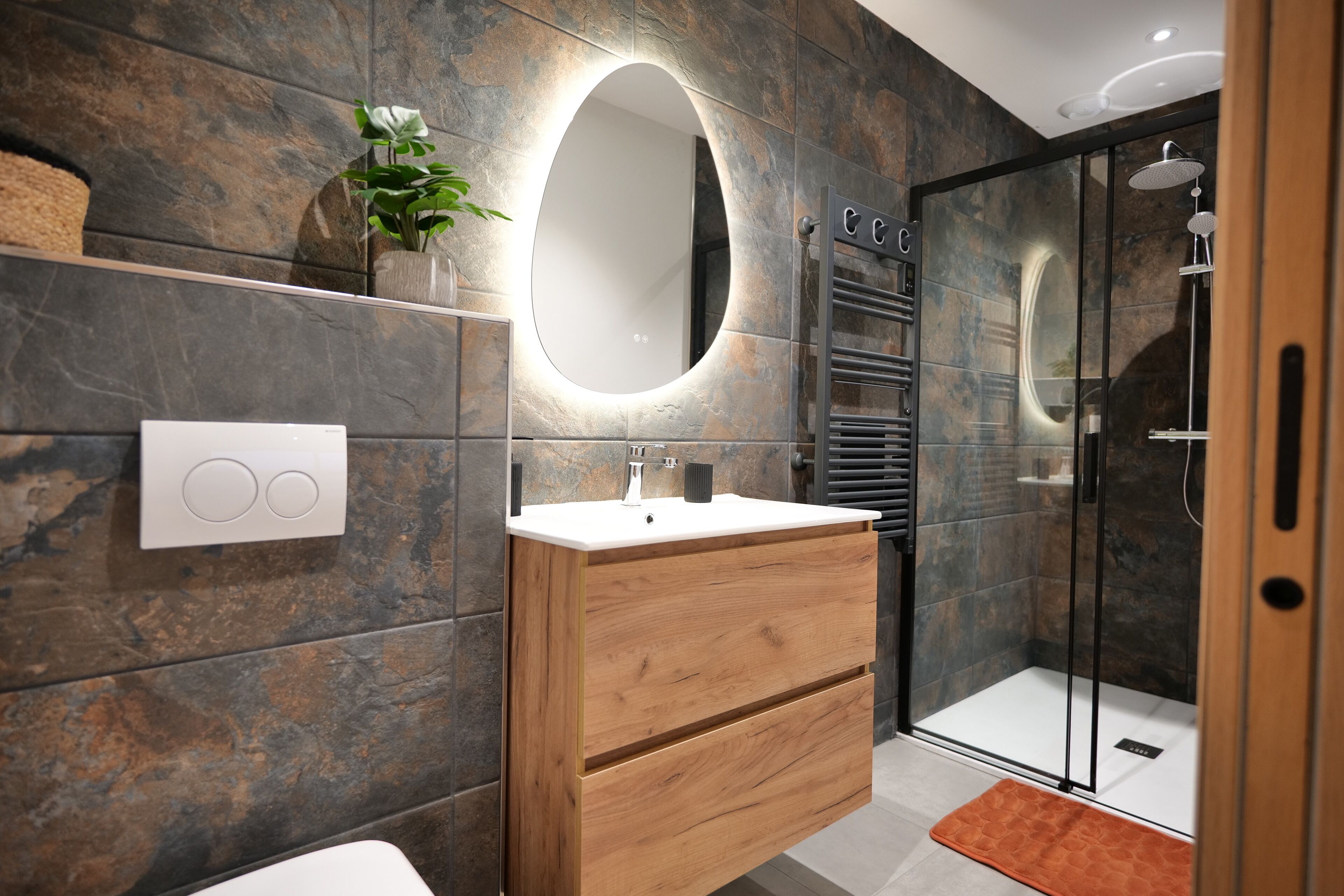 Une salle de bain moderne avec un meuble-lavabo en bois, un grand miroir ovale et une cabine de douche en verre.